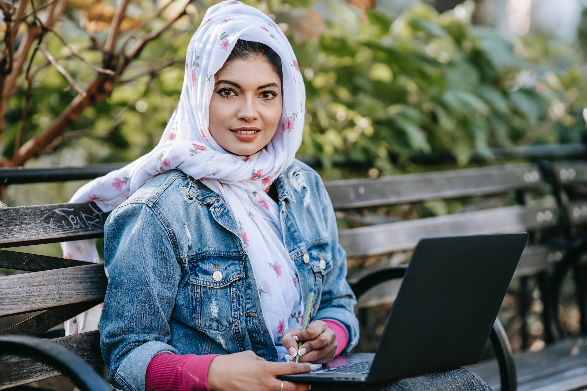 muslim woman writing information while working on laptop